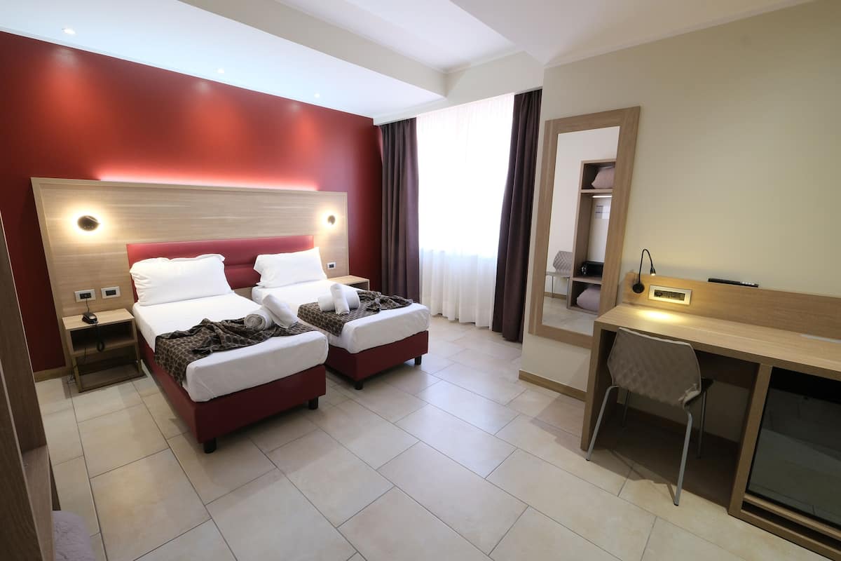 A hotel room with two beds, a desk, a chair, and a mirror.