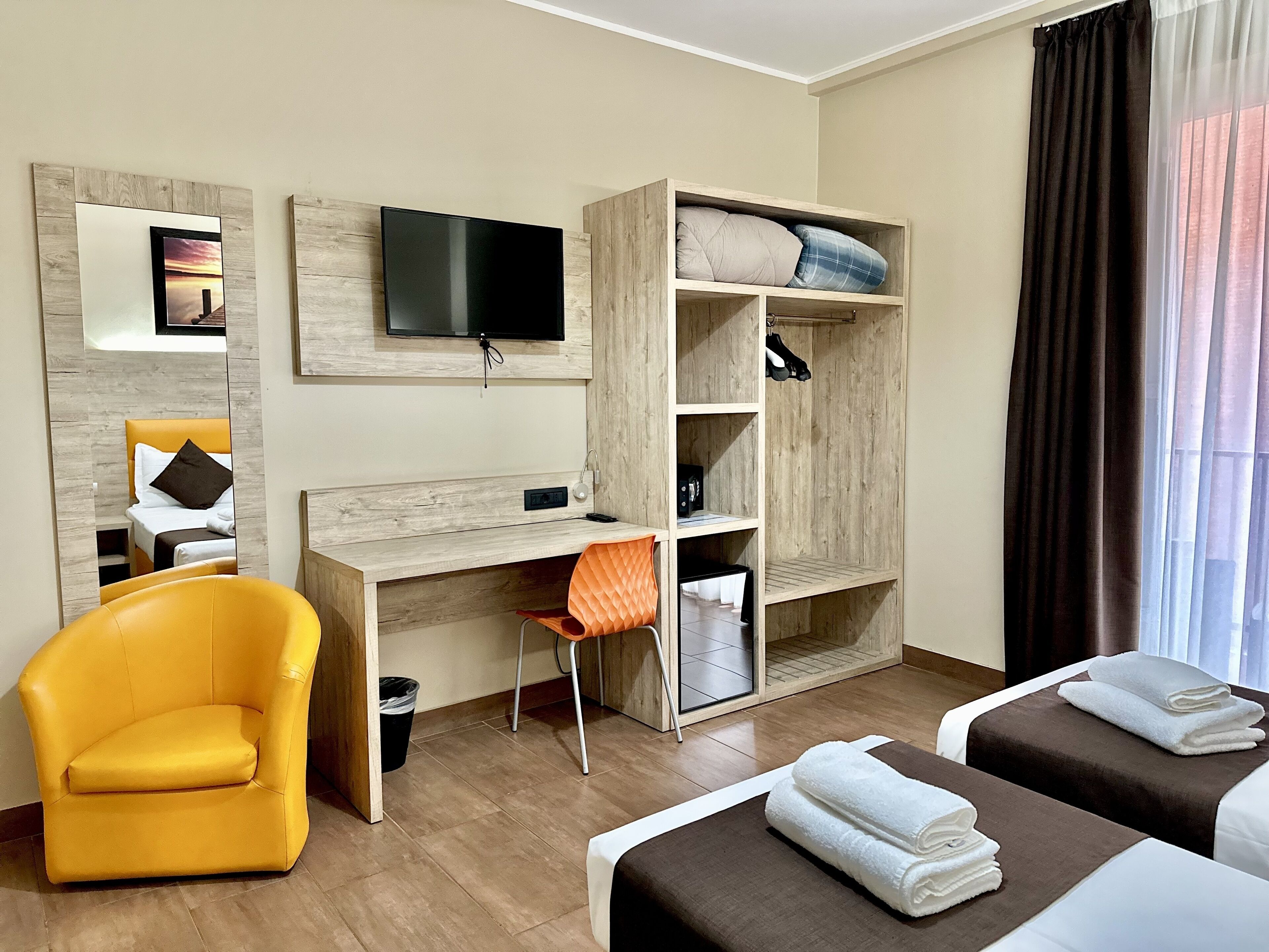 Ein Hotelzimmer mit Bett, Schreibtisch, Sessel, Fernseher und Kleiderschrank.