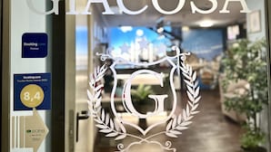 Entrada de un hotel con el nombre "HOTEL GIACOSA" y un logotipo con una corona y estrellas. Se exhiben premios en la pared, incluyendo una calificación de 8.4 de Booking.com y el Premio a los Viajeros 2020.