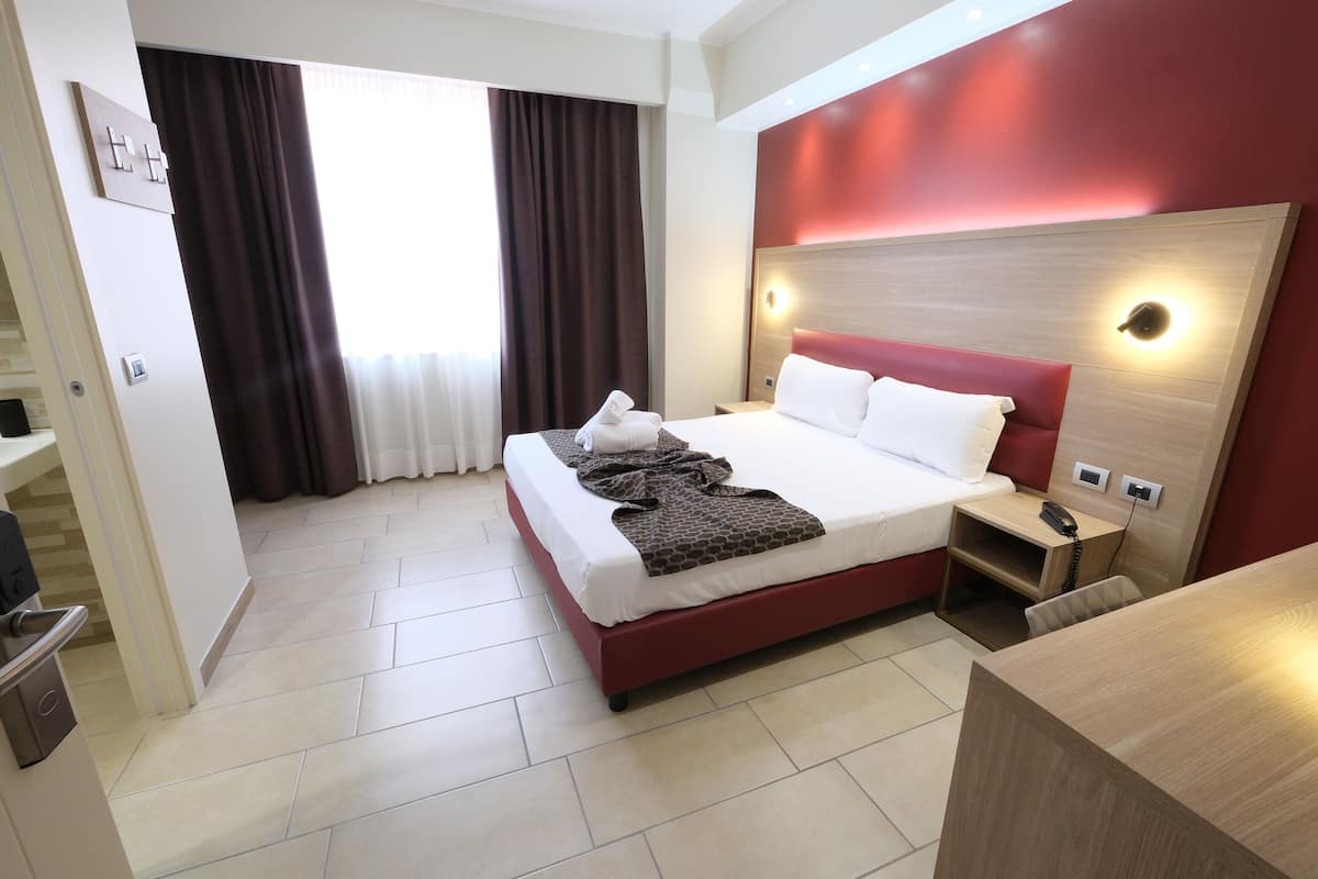 A hotel room with a bed, bedside table, and a desk.