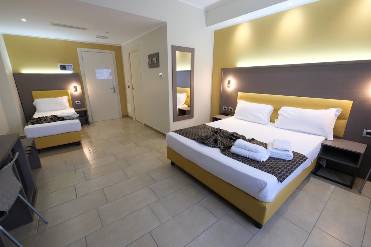 A hotel room with two beds, a desk, a chair, a mirror, and a door.