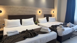 Habitación de hotel con dos camas, cada una con ropa blanca y almohadas, una manta estampada en una cama y toallas en la otra.