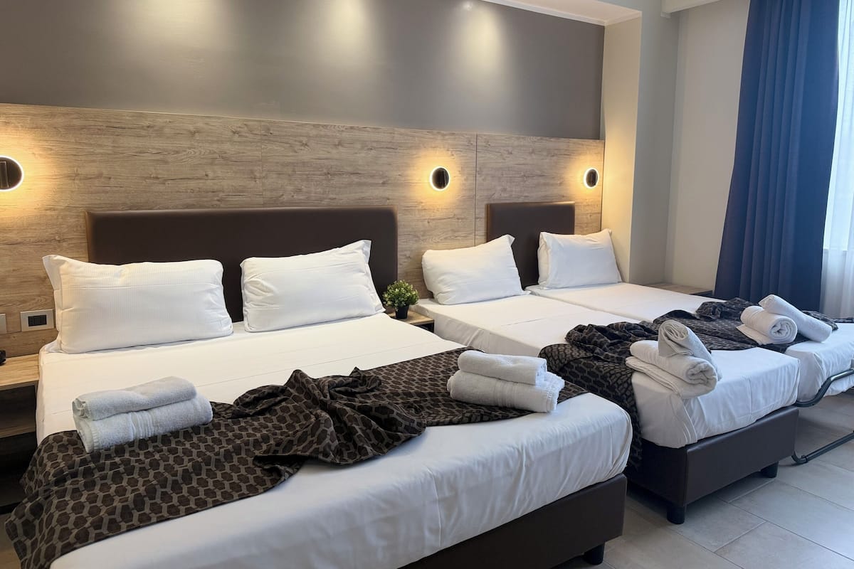 A hotel room with two beds, each with white linens and pillows, a patterned blanket on one bed, and towels on the other.