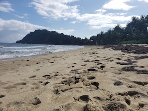 A sandy beach with footprints, a clear sky, and a distant hill.