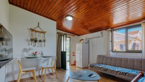 Una sala de estar moderna con techo de madera, un sofá, una mesa de comedor con sillas y una zona de cocina con refrigerador.