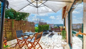 Un patio al aire libre con piso de piedra, sillas de madera, una mesa y un paraguas grande.