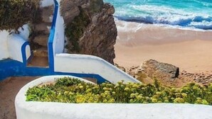 Una escalera costera que baja a una playa con aguas azules y transparentes.