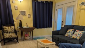 Een woonkamer met houten vloer, een bank, een fauteuil, een klein tafeltje en een lamp.
