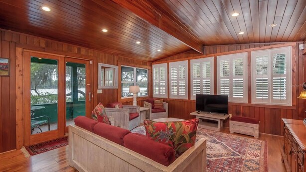 A cozy cabin interior with a wooden ceiling, large windows with shutters, a sofa set, a television, and a dining table. - Lakefront Country Haven near Ocala & Forest -With Canoe, Lifejackets and Grill! (Ft McCoy)