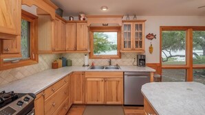 A kitchen with wooden cabinets, a stainless steel sink, and a dishwasher. There is a window with a view of trees and a body of water. - Lakefront Country Haven near Ocala & Forest -With Canoe, Lifejackets and Grill! (Ft McCoy)