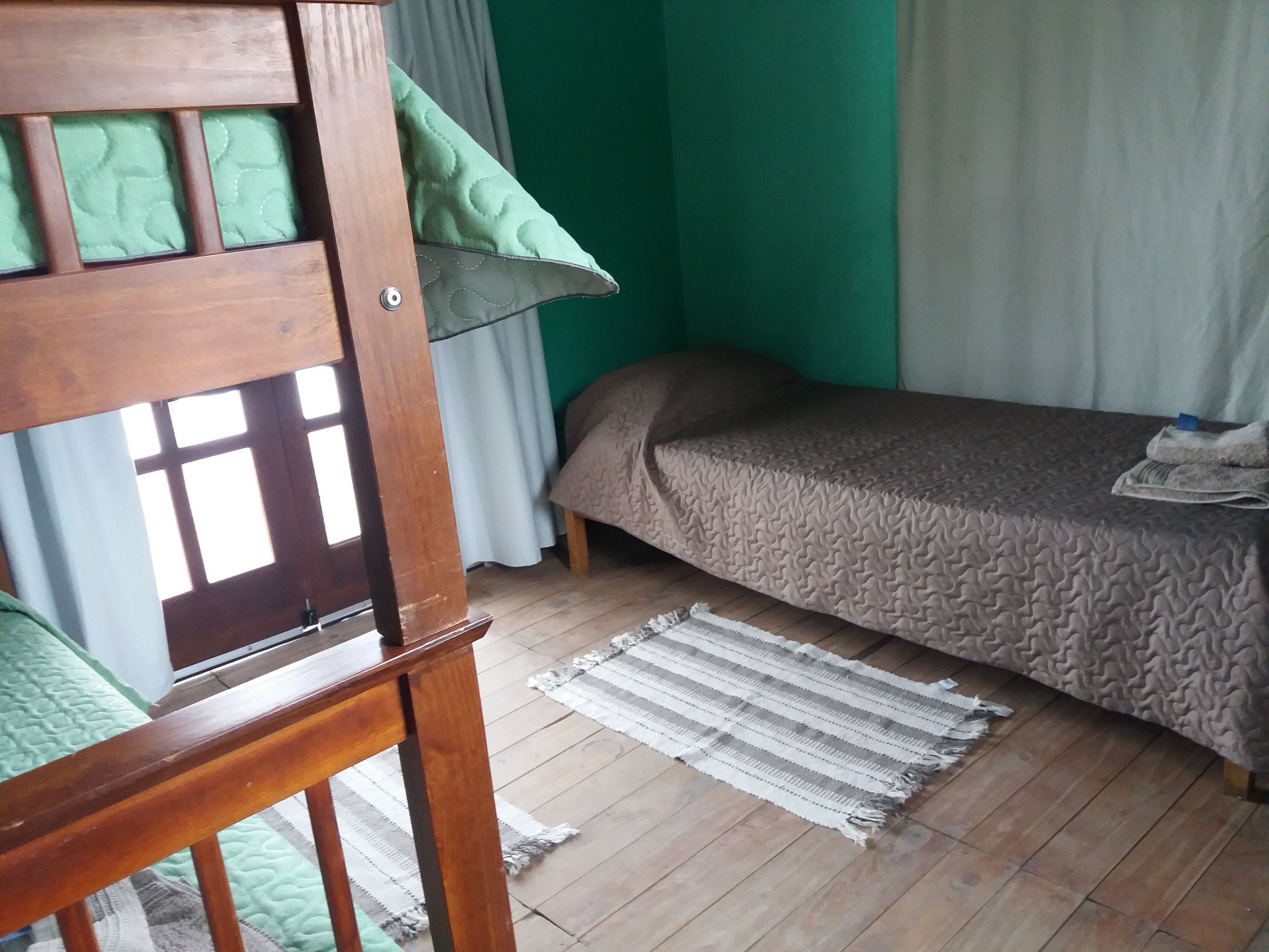 Ein Zimmer mit Etagenbett, einem Einzelbett, Holzboden und grüner Wand.