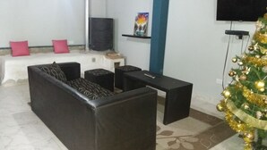 A living room with a sofa, a coffee table, and a TV. There is a Christmas tree with decorations.