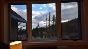 A room with a large window overlooking a forested area, a heater, and a lamp. - Sherpa Studio (Whitefish)