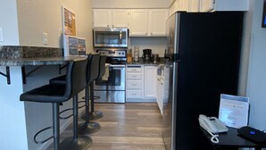 A compact kitchen with white cabinets, stainless steel appliances, and a black refrigerator. - Sherpa Studio (Whitefish)