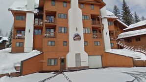 A multi-story wooden lodge with balconies, a ski lift, and a snowy landscape. - Sherpa Studio (Whitefish)