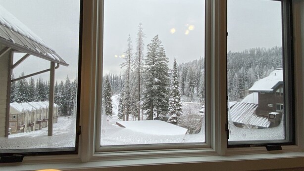 A room with a large window overlooking a snowy landscape with trees and buildings. - Sherpa Studio (Whitefish)