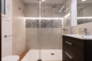 A modern bathroom with a glass-enclosed shower, a white toilet, and a dark wooden vanity with a mirror.