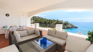 A balcony with wicker furniture, a glass table, and a view of the sea and greenery. - Charming house with sea views in Salou 015 Casas Blancas (Salou)