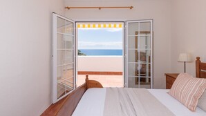 A bedroom with a bed, a nightstand, a lamp, and an open door leading to a balcony with a view of the sea. - Charming house with sea views in Salou 015 Casas Blancas (Salou)