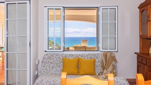 A room with a sofa, a window with a view of the sea, and a wooden cabinet. - Charming house with sea views in Salou 015 Casas Blancas (Salou)
