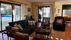 Un salon spacieux comprenant un canapé, des fauteuils et une table basse. De grandes portes-fenêtres coulissantes donnent accès à un patio avec une piscine.