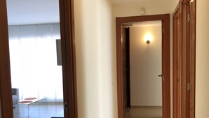 Un pasillo con puertas de madera, suelo de baldosas y una lámpara en el techo.