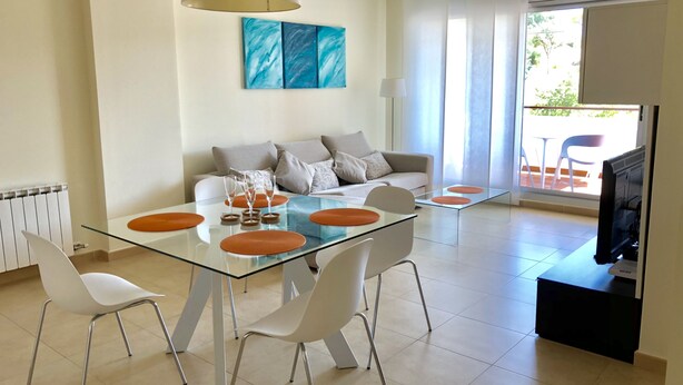Una sala de estar moderna con una mesa de comedor de vidrio, sillas blancas, un sofá y un televisor.