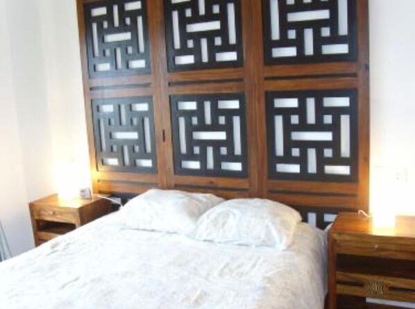 Una habitación con una cama, cabecera de madera con diseños geométricos y dos mesitas de noche con lámparas.