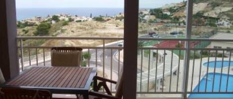 A balcony with a table and chairs, overlooking a coastal town and a swimming pool.