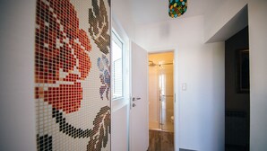 Un pasillo con pared de azulejos, puerta de ducha de cristal y suelo de madera.