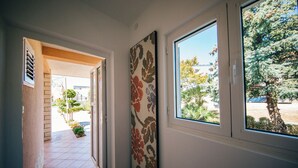 Un pasillo con piso de baldosas, una puerta que da al exterior y una ventana con vista a árboles y un coche estacionado.