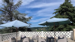 An outdoor patio with plastic chairs and umbrellas, a white lattice fence, and a view of a green landscape.