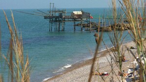 A beach with a pier extending into the water, a few people on the shore, and some beach chairs and umbrellas.