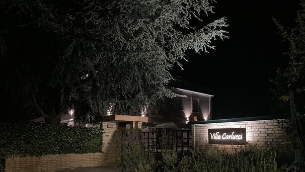 Villa Carlucci with a brick entrance, illuminated signage, and a pathway leading to the building.