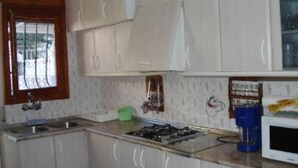 Una cocina con armarios blancos, un reloj en la pared, una ventana con barrotes y un microondas.