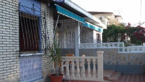 Un edificio con fachada de tejas, un balcón con barandilla y una planta en maceta.