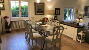 A dining area with a glass table and chairs, a radiator, and a window with a view of greenery. - Charming Villa with pool near Rome  (Sacrofano)