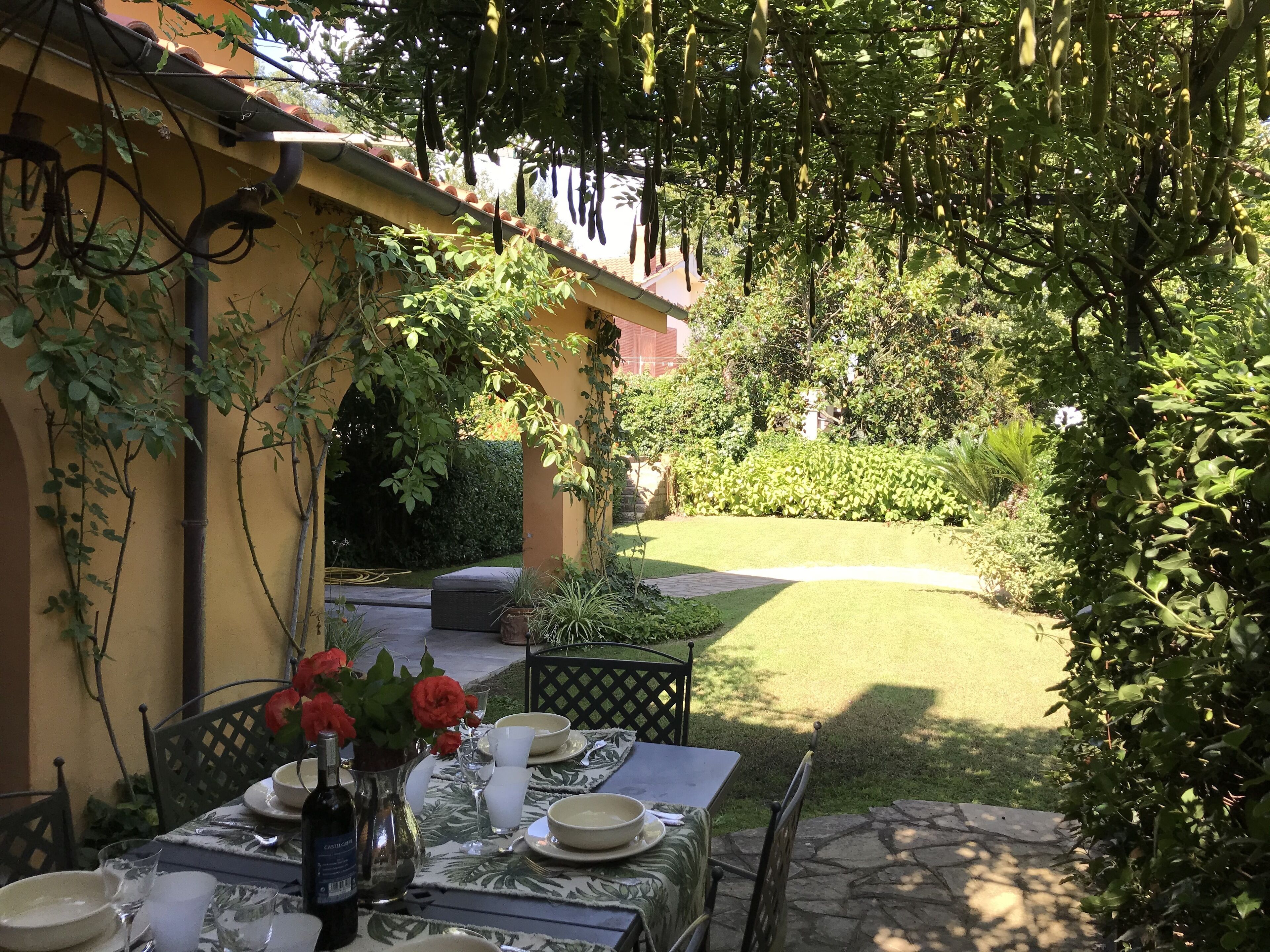 Un área de comedor al aire libre con una mesa dispuesta para dos personas, rodeada de follaje y un césped cuidado.