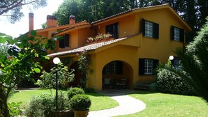 A yellow house with a garden, a paved path, and a bench. - Charming Villa with pool near Rome  (Sacrofano)