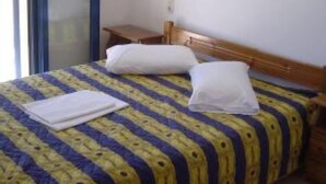 A bedroom with a bed, a nightstand, and a small wall-mounted lamp. - Complex of apartments & studio, full-equipped, in a large, beautiful garden (Kamilari)