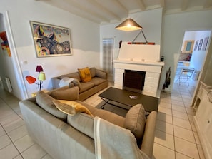 A living room with a sofa, a coffee table, a fireplace, and a painting on the wall. - Wooden house in Cap Ferret with big garden A0353 (Lège-Cap-Ferret)