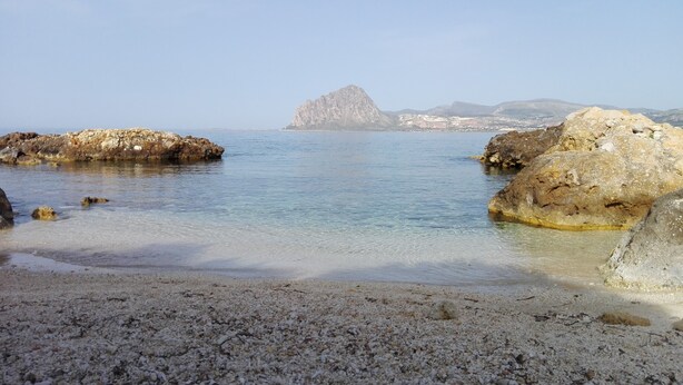 Una playa de guijarros con agua cristalina y formaciones rocosas.