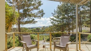 Un balcón con dos sillas, una mesita y vista a un lago y árboles.