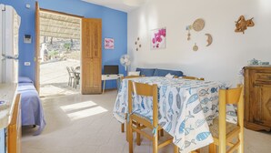 Una habitación con pared azul, una puerta de madera que da al exterior, una mesa de comedor con mantel estampado con motivos de peces y un mueble de madera.