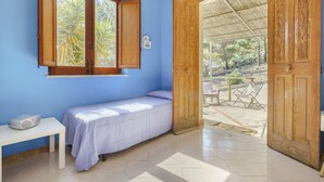 Una habitación pequeña con una cama individual, una ventana, una mesa y una puerta que da a un espacio al aire libre.