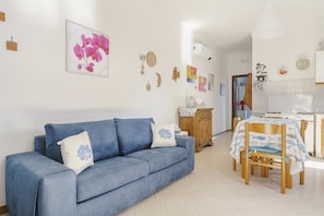 A living room with a blue sofa, a dining table with chairs, and a kitchen in the background. - Beautiful location overlooking the sea. (Erice)