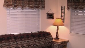 A cozy living room with a patterned sofa, a wooden coffee table, and a lamp on a side table. - Bear Trap Apartments - Full Kitchen (Gardiner)