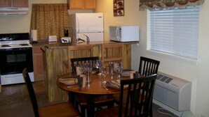 A compact kitchen with a stove, microwave, and refrigerator. There is a dining table with chairs and a window with blinds. - Bear Trap Apartments - Full Kitchen (Gardiner)