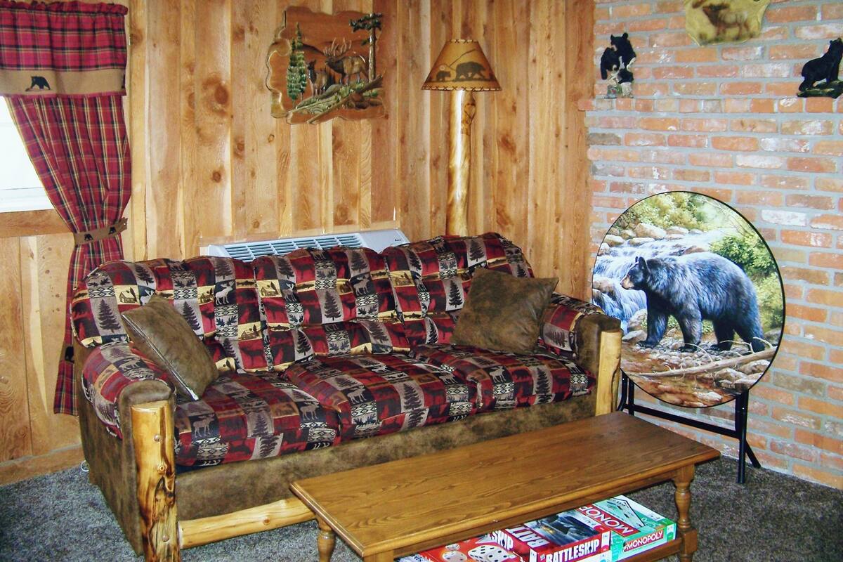 A cozy room with a wooden wall, a plaid-patterned sofa, a wooden coffee table, and a bear-themed welcome sign.