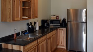 A kitchen with wooden cabinets, a stainless steel refrigerator, a microwave, and a sink. - Bear Trap Apartments - Full Kitchen (Gardiner)